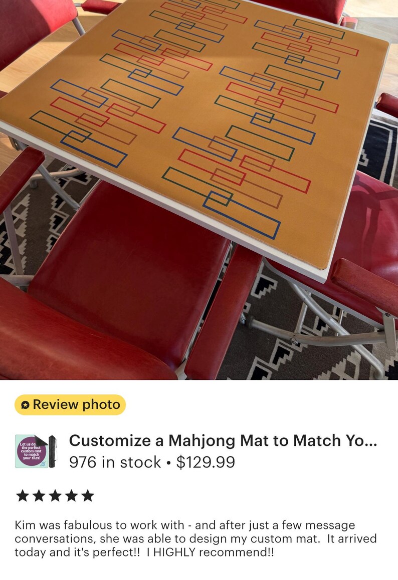 May include: A custom mahjong mat with a tan surface and a white border. The mat features a geometric design of red and blue rectangles. Red chairs surround the table.