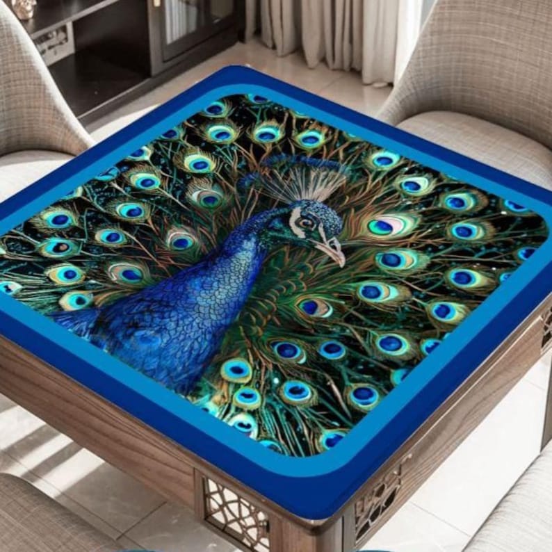 Puede incluir: Un mantel cuadrado que presenta un pavo real vibrante con una cola en abanico de plumas azules y verdes iridiscentes. El dise&ntilde;o muestra patrones detallados en forma de ojo en todo el plumaje, enmarcado por un borde azul oscuro s&oacute;lido.