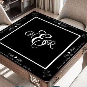 May include: A square black mahjong table mat featuring a white border and a central white monogram of the letters H and E. The mat includes white text printed along the edges with directional instructions and game terminology in English.