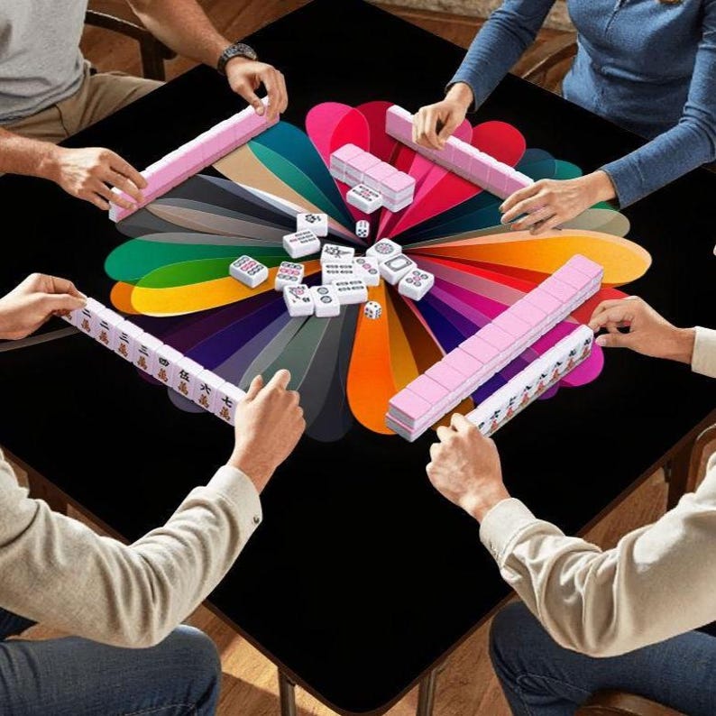 Puede incluir: Una partida de Mahjong en una mesa negra. La mesa tiene un dise&ntilde;o floral colorido en el centro. Las fichas de Mahjong son blancas con s&iacute;mbolos negros, y los soportes son rosas. Tambi&eacute;n se ven dados.