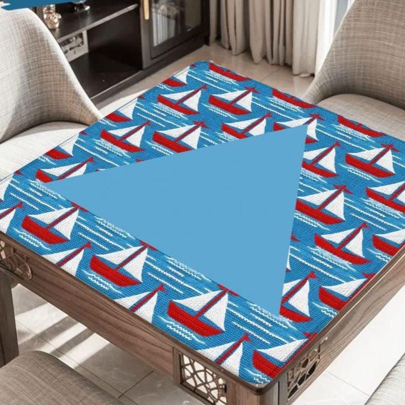 May include: A wooden table with a blue and white nautical-themed tablecloth. The tablecloth features a pattern of red sailboats on a blue background. A large, light blue triangle is in the center of the table.