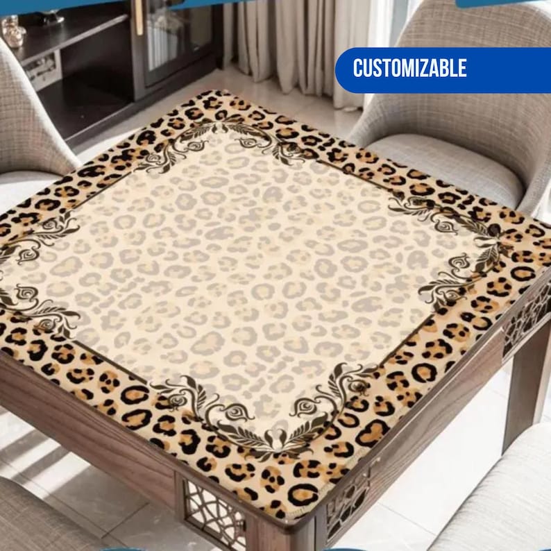 May include: A square table cover with a leopard print border and a light beige center. The border features a brown and black leopard pattern with decorative floral accents. The center has a subtle leopard print. The table cover is on a wooden table, and the word 'CUSTOMIZABLE' is visible in a blue banner.