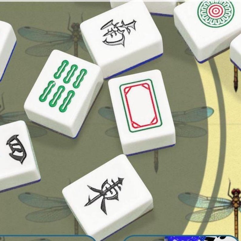 May include: A collection of white Mahjong tiles with various symbols and markings in green, red, and black. The tiles are arranged on a green surface with dragonfly illustrations. The tiles have blue edges.