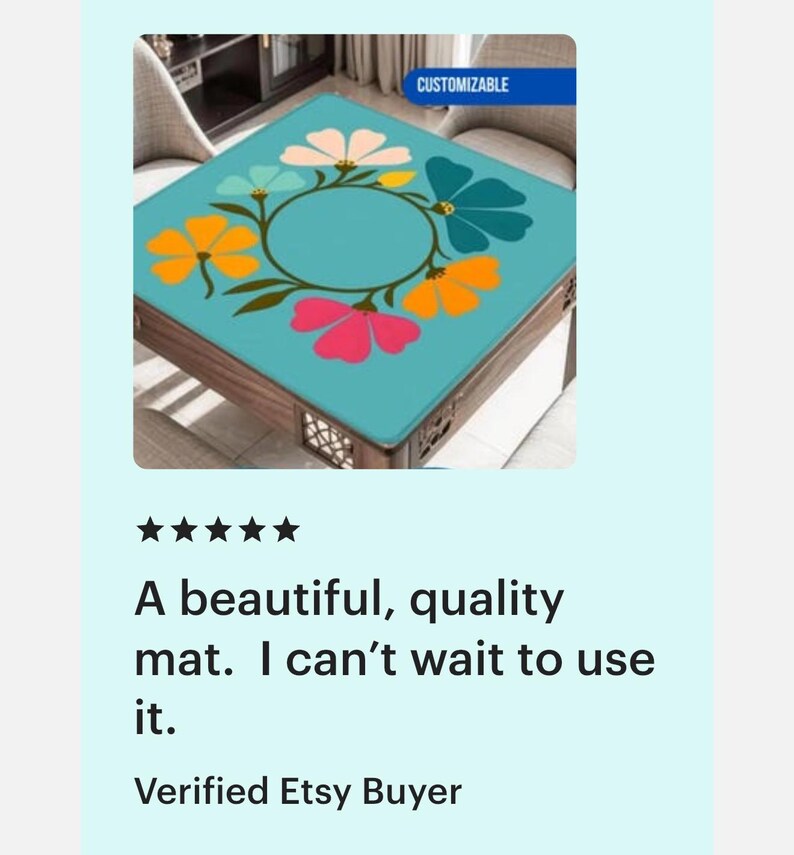 May include: A square table mat with a teal background and a floral design. The flowers are in shades of pink, orange, white, and teal, arranged in a circular pattern. The mat is on a wooden table. The word "CUSTOMIZABLE" is in a blue rectangle.