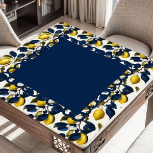 May include: A rectangular table cover with a navy blue center and a border featuring a lemon and leaf pattern. The lemons are yellow, and the leaves are dark blue against a white background. The table is made of wood.