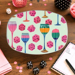 May include: An oval-shaped tray featuring a light green background with a repeating pattern of pink dice and various colorful stemmed glasses. The glasses are depicted in shades of pink, blue, orange, and green, scattered among the dice.