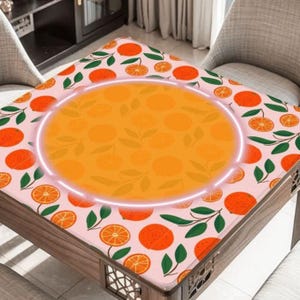 May include: A square table with a pink tablecloth featuring a pattern of oranges, orange slices, and green leaves. The center of the table has a large orange circle with a white glowing outline. The table is made of wood.