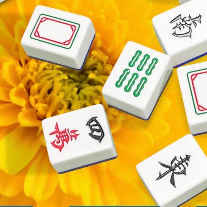 Puede incluir: Fichas de Mahjong blancas con bordes azules y varios s&iacute;mbolos en rojo, verde y negro. Las fichas est&aacute;n dispersas sobre un fondo de flores amarillas. Los s&iacute;mbolos incluyen caracteres chinos y conjuntos de l&iacute;neas verdes.