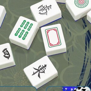 Op de afbeelding: Witte Mahjong-tegels met verschillende groene en zwarte symbolen en tekens. Sommige tegels tonen sets van drie groene stippen, terwijl andere ingewikkelde zwarte symbolen weergeven. De tegels zijn gerangschikt op een patroon.