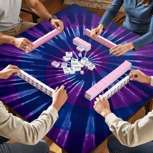 May include: A square mahjong table cover featuring a vibrant purple and blue tie-dye pattern. Four players are seated around the table, each with a rack of mahjong tiles. A collection of white mahjong tiles and two small dice are in the center.