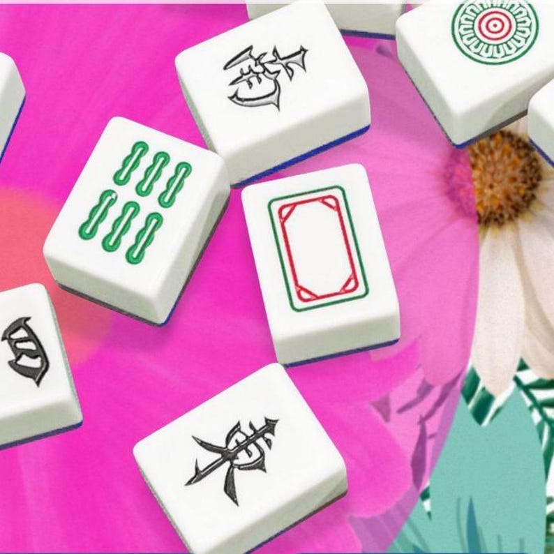 May include: A collection of white Mahjong tiles with various symbols and markings in green, red, and black. The tiles are arranged on a vibrant pink surface, with a hint of a white flower in the background. The game pieces are rectangular and have blue edges.