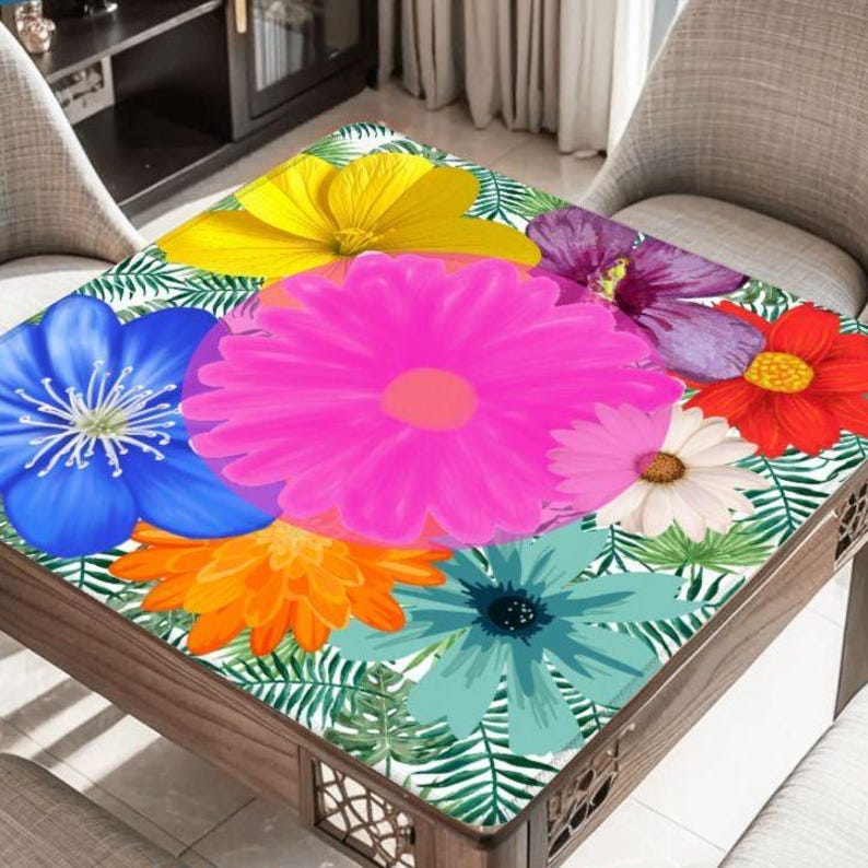 May include: A square wooden table with a floral design. The tabletop features a vibrant arrangement of large, colorful flowers in shades of pink, yellow, blue, orange, and red, set against a white background with green leaves.