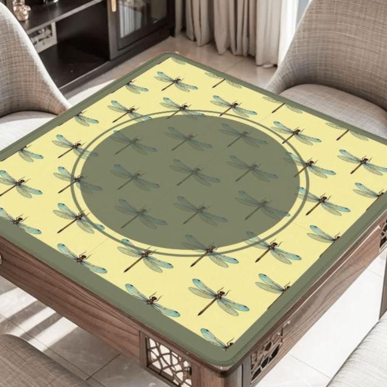 May include: A square table with a light yellow surface featuring a dragonfly pattern. The center has a large, dark green circle with more dragonflies. The table has a dark wood frame and decorative cutouts.