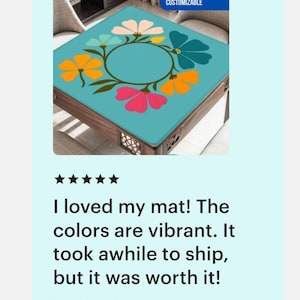 May include: A square table mat with a teal background and a floral design in pink, orange, yellow, and teal. The mat is customizable, as indicated by the text in the upper right corner.