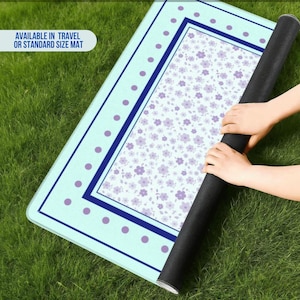 May include: A rolled-up floral mat with a light blue border and a floral pattern in the center. The mat has a dark blue border and purple polka dots. The text "AVAILABLE IN TRAVEL OR STANDARD SIZE MAT" is visible.