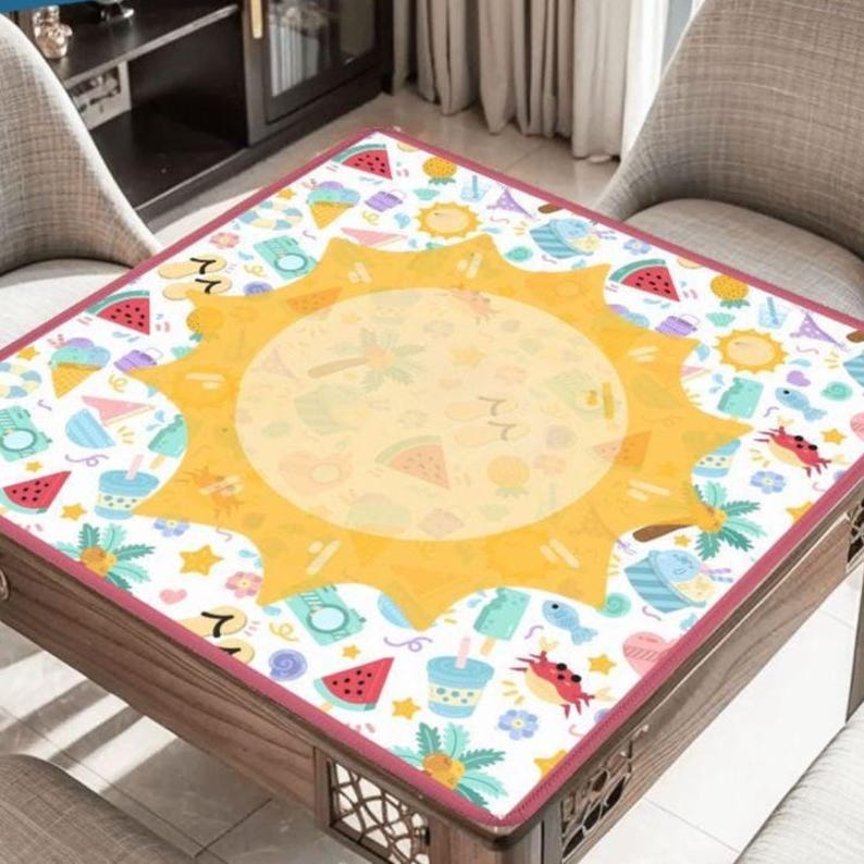 May include: A square table cover featuring a large yellow sun in the center surrounded by a repeating pattern of summer icons including watermelon slices, ice cream cones, crabs, flip-flops, palm trees, and cameras on a white background.
