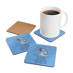 Puede incluir: Una taza blanca llena de café se encuentra sobre un posavasos azul con un diseño de dragón de dibujos animados. El posavasos tiene el texto "GOT A DRAGON, A FEW FLOWERS AND A NORTH WIND. MY MAH JONGG HAND NEEDS SOME WORK!" También se muestran dos posavasos adicionales y un posavasos de corcho.