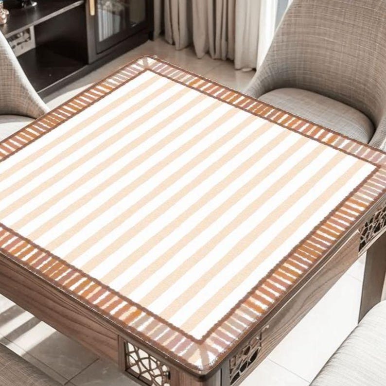 Pu&ograve; includere: Un tavolo quadrato in legno con un piano a righe beige e bianco. Il tavolo ha un bordo decorativo e dettagli intagliati sui lati. Il tavolo &egrave; circondato da due sedie imbottite.