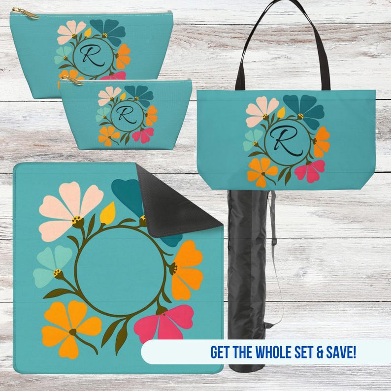 May include: A set of turquoise accessories featuring a floral wreath design with the letter "R". The set includes a tote bag, two cosmetic bags, and a blanket. The tote bag has black handles, and the blanket is folded with a black underside.