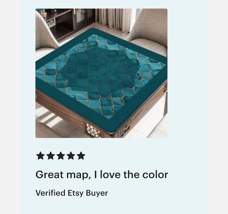 May include: A square table mat featuring a teal and dark blue Moroccan-style quatrefoil pattern with thin gold outlines. The mat has a solid dark teal border and is positioned on a wooden table surface with a lattice-style base design.