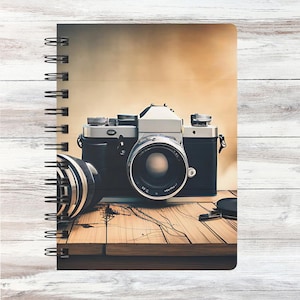May include: A vintage camera with a black leather case and a silver lens sits on a wooden surface. The camera has a silver body and a black lens with a silver ring around it. The camera is in focus and the background is blurred.