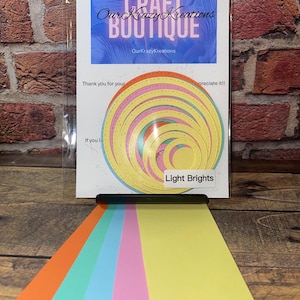 May include: A set of 7 paper crafting dies in various sizes, featuring a circle design with a stitched edge. The dies are in shades of yellow, pink, and orange. The dies are labeled "Light Brights".