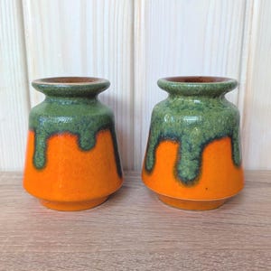 Pode incluir: Dois vasos de cerâmica com um design distinto. Os vasos apresentam uma base laranja vibrante, passando para uma cobertura verde escorrida no topo. As bordas são marrons mais escuras. Estes vasos decorativos são adequados para exibir flores ou como decoração.