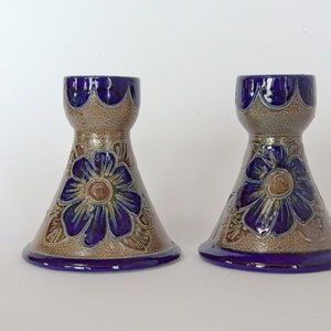 Puede incluir: Un par de candelabros de cerámica con un diseño floral azul y marrón. Los candelabros tienen la forma de un jarrón con una base ancha y un cuello estrecho.
