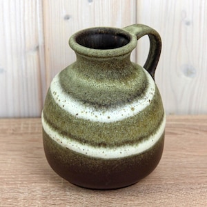 May include: A ceramic vase with a handle, featuring a rounded body and a dark brown base. The vase has a green and white striped pattern, with a dark brown interior and handle. The vase is likely used for decorative purposes.
