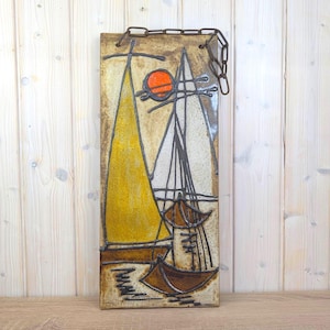 Puede incluir: Arte mural rectangular de cerámica con una escena de veleros. La obra de arte representa dos veleros con velas amarillas y blancas, un sol naranja y cascos de barco marrones. Se adjunta una cadena de metal para colgar.