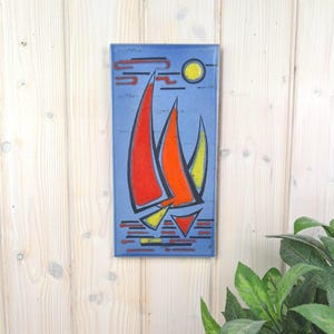 Könnte beinhalten: Eine rechteckige Wandplatte mit einem stilisierten Emaille-Design von drei Segelbooten auf blauem Grund. Die Segel sind in leuchtendem Rot, Orange und Gelb gehalten, mit einer gelben Sonne in der oberen rechten Ecke und horizontalen Linien.