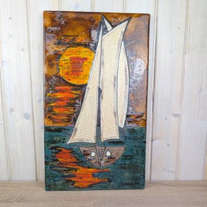 May include: Rectangular ceramic wall art depicting a sailboat on the water at sunset. The sailboat has white sails and a brown hull. The sun is a large yellow circle, and the water is teal and orange.