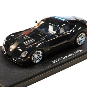 Può includere: Un modellino di auto 2010 Devon GTX nero dal design aerodinamico e ribassato, con cerchi argentati a più razze, cofano ventilato e fari trasparenti. Il veicolo in miniatura è montato su una base rettangolare nera con la scritta 2010 Devon GTX.