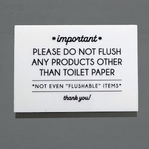 May include: A roll of white toilet paper on a chrome holder next to a white sign with black text that reads "*important* PLEASE DO NOT FLUSH ANY PRODUCTS OTHER THAN TOILET PAPER *NOT EVEN "FLUSHABLE" ITEMS* thank you!"