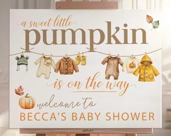 May include: A canvas sign on a wooden easel with the text "a sweet little pumpkin is on the way" and "welcome to BECCA'S BABY SHOWER". The sign features illustrations of baby clothes and a pumpkin.