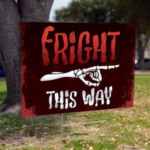 May include: A rectangular sign with the words "FRIGHT THIS WAY" in red and white, with a skeleton hand pointing to the right. The sign is on a metal stake, set in grass, with a tree in the background.
