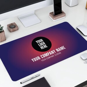 May include: A blue and red gradient desk mat with a black circle containing the text "YOUR LOGO HERE" and the text "YOUR COMPANY NAME YOUR COMPANY SLOGAN" in white.