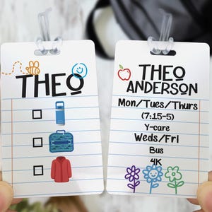 May include: Two rectangular white plastic bag tags with clear plastic loops. The left tag features the name THEO, a bee, a smiley face, and a checklist with icons for a water bottle, lunch bag, and jacket. The right tag displays THEO ANDERSON, an apple, a weekly schedule, and three colorful flower illustrations.