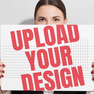 May include: A person holding a white sign with the words "UPLOAD YOUR DESIGN" in large red letters. The sign has horizontal lines and a grid pattern. The background is a plain, light gray.