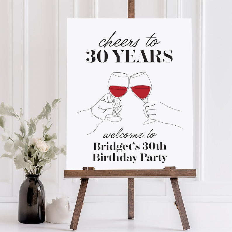 May include: A white sign with black text that reads 'cheers to 30 YEARS' and 'welcome to Bridget's 30th Birthday Party'. The sign has a drawing of two wine glasses clinking with red wine in them.