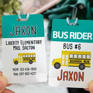 May include: Two rectangular school bus tags. One tag has the name "JAXON" at the top, followed by "LIBERTY ELEMENTARY" and "MRS. SALTON". The other tag says "BUS RIDER" and "BUS #6". Both tags feature a yellow school bus graphic.