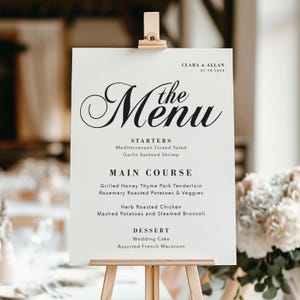 May include: A white wedding menu sign with black text. The menu includes starters, main course, and dessert options. The text reads "Clara & Allan 07.18.2024 The Menu Starters Mediterranean Tossed Salad Garlic Sauteed Shrimp Main Course Grilled Honey Thyme Pork Tenderloin Rosemary Roasted Potatoes & Veggies Herb Roasted Chicken Mashed Potatoes and Steamed Broccoli Dessert Wedding Cake Assorted French Macarons"
