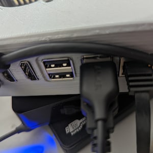 Könnte beinhalten: Nahaufnahme eines weißen Plastikgehäuses mit mehreren schwarzen Kabeln, die an der Rückseite eingesteckt sind. Das Gehäuse hat drei USB-Anschlüsse und einen schwarzen Ethernet-Anschluss.