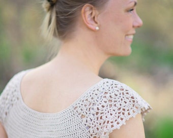 May include: A woman wearing a crocheted top with a delicate lace pattern on the sleeves. The top is a light beige color and has a scoop neckline.