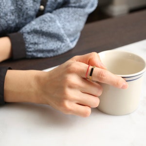 May include: A gold ring with a black rectangular band, worn on a finger with a red rubber band.