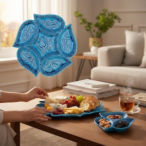 Könnte beinhalten: Ein Set aus türkisfarbenen Keramik-Servierschalen mit floralem Design. Das Set umfasst eine große, blütenförmige Platte und kleinere, blattförmige Schalen. Die Platte ist mit Käse, Trauben und Brot gefüllt. Auf dem Tisch steht eine Tasse Tee.