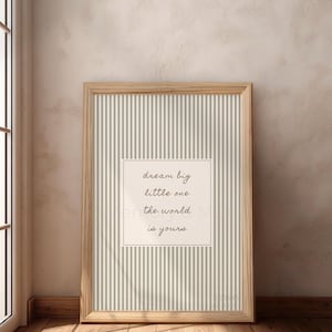 May include: A framed print with a light wood frame. The print has a striped background with the words "dream big little one the world is yours" in a white square.