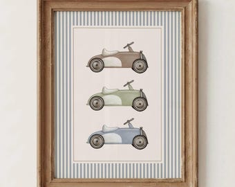 May include: A framed wall art print featuring three vintage-style toy pedal cars in brown, sage green, and dusty blue, arranged vertically on a cream background. The print is bordered by a blue and white vertical striped pattern in a wooden frame.