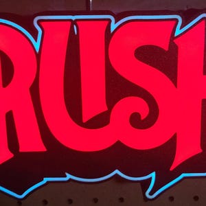 May include: A red neon sign with the word "RUSH" in a stylized font. The letters are outlined in blue.