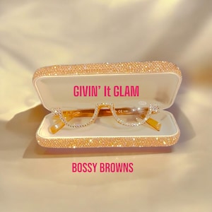 Könnte beinhalten: Eine goldene Brille mit klaren Gläsern und Strasssteinen in einem glitzernden rosa und weißen Etui. Das Etui trägt den Text "GIVIN' It GLAM" und "BOSSY BROWNS".